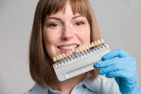 Primer plano del dentista utilizando una guía de sombra en la boca de la mujer para comprobar la chapa de dientes en busca de blanqueamiento o nuevas piezas de dentadura postiza