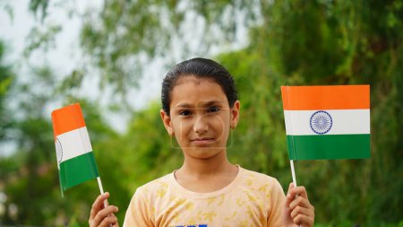 Photo for Cute Indian girl holding Indian flag in her hand and smiling. Celebrating Independence day or Republic day in India. A girl showing pride of Tiranga - Royalty Free Image