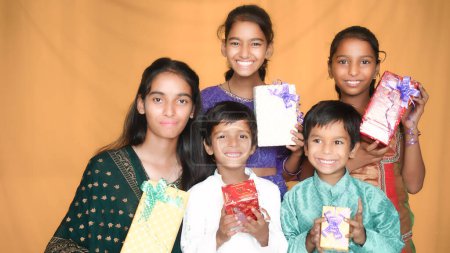 Téléchargez les photos : Heureux jeunes enfants indiens échanger des boîtes-cadeaux célébrant le festival diwali ensemble isolé sur fond de studio - en image libre de droit