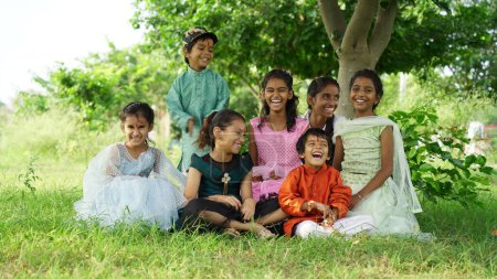 Téléchargez les photos : Frères et sœurs indiens célébrant le festival Raksha Bandhan ou Rakhi au jardin tout en portant des vêtements traditionnels et assis sur fond de nature - en image libre de droit