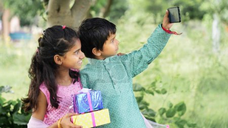 Foto de Hermanitos en ropa étnica tomando selfie con motivo de las celebraciones del festival Raksha bandhan - Imagen libre de derechos