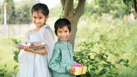 Foto de Hermano y hermana hindúes en ropa étnica sosteniendo dulces indios y caja de regalo con motivo del festival Raksha Bandhan - Imagen libre de derechos