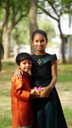 Téléchargez les photos : Frère et sœur hindous en tenue ethnique tenant bonbons indiens et coffret cadeau à l'occasion du festival Raksha Bandhan - en image libre de droit