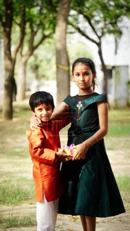 Téléchargez les photos : Frère et sœur hindous en tenue ethnique tenant bonbons indiens et coffret cadeau à l'occasion du festival Raksha Bandhan - en image libre de droit