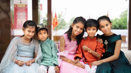 Téléchargez les photos : Frères et sœurs indiens célébrant le festival Raksha Bandhan ou Rakhi au jardin tout en portant des vêtements traditionnels et assis sur fond de nature - en image libre de droit