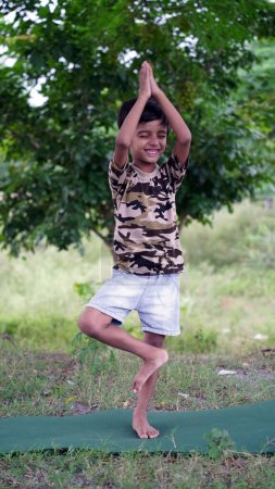 Foto de Retrato de un chico guapo practicando yoga al aire libre. Hermoso niño practica yoga asana o hace ejercicios gimnásticos. Niños meditando en posición de loto - Imagen libre de derechos