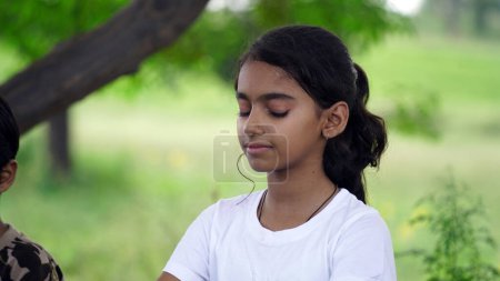 Téléchargez les photos : Charmante petite fille qui fait une méditation sérieuse de yoga dans le jardin. Petite fille indienne enfant faire de la méditation - en image libre de droit