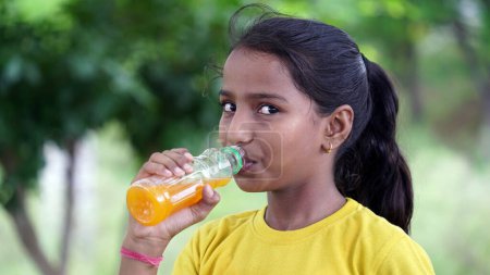 Photo for Girl drinking juice. Asian kid drinking from plastic bottle. Portrait of a girl drinking orange juice. Orange juice in bottle. People drink energy drink. child tasting drink from plastic bottle. - Royalty Free Image