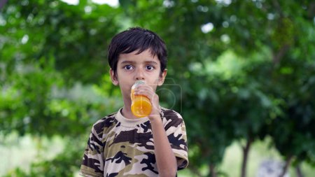 Foto de Chico bebiendo jugo. Niño asiático bebiendo de botella de plástico. Retrato de un chico bebiendo jugo de naranja. Jugo de naranja en botella. La gente bebe bebida energética. bebida degustación infantil de frasco de plástico. - Imagen libre de derechos
