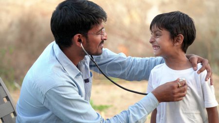 Photo for Indian young village doctor of pediatrician holding stethoscope checking heartbeat of sick boy kid. health checkup, children medical insurance care. healthcare Concept - Royalty Free Image