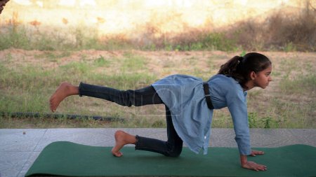 Téléchargez les photos : Charmante petite fille qui fait une méditation sérieuse de yoga dans le jardin. Petite fille indienne enfant faire de la méditation - en image libre de droit