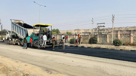 Téléchargez les photos : Le chantier de construction pose une nouvelle chaussée de route asphaltée. Travailleur utilisant une machine de revêtement d'asphalte pendant les travaux de construction et de réparation de routes. Sikar, Rajasthan, Inde - février 2024 - en image libre de droit