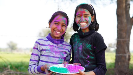 Téléchargez les photos : Joyeuses jeunes filles indiennes jouant des couleurs, souriant avec des couleurs sur le visage ou des enfants asiatiques célébrant Holi. Concept pour le festival indien Holi. Enfants brillants enduits de poudre colorée - en image libre de droit