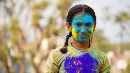 Téléchargez les photos : Jeune enfant mignon gai petite fille avec poudre de couleurs holi appliquées montrant les mains colorées à la caméra pendant la célébration du festival holi - en image libre de droit