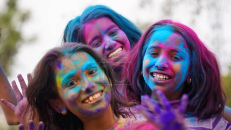 Téléchargez les photos : Jeune enfant mignon gai petite fille avec poudre de couleurs holi appliquées montrant les mains colorées à la caméra pendant la célébration du festival holi - en image libre de droit