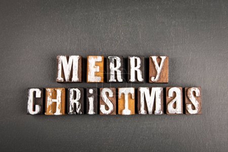 Photo for Merry Christmas. Text from wooden alphabet blocks on a dark chalkboard background. - Royalty Free Image