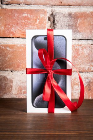 Photo for Sigulda, Latvia - October 18, 2023: Box of the Iphone 15 Pro on a red brick background. Gift with a red ribbon - Royalty Free Image