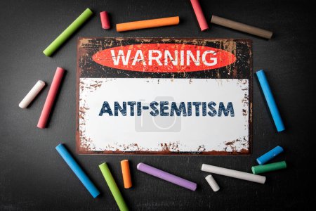 Photo for Anti-Semitism. Metal warning sign and colored pieces of chalk on a dark chalkboard background. - Royalty Free Image