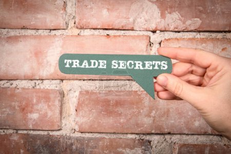 Trade Secrets. Green speech bubble with text on a red brick background.