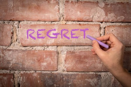REGRET. Text written with purple chalk on a red brick background.