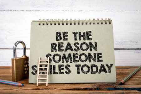 Sei der Grund, warum jemand heute lächelt. Grüner Notizblock auf Holztisch und weißem Hintergrund.