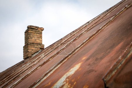 Photo for Old rusty metal roof with patches. Repair and renovation. Brick chimney. - Royalty Free Image