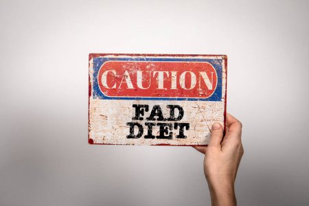 Fad Diet. Metal warning sign in a womans hand on a white background.