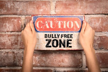 Bully Free Zone. Caution sign in a womans hand on a brick background.