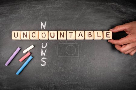 Uncountable nouns. Wooden block crossword puzzle and pieces of chalk on a chalkboard background.