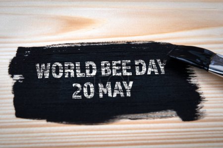 World Bee Day 20 May. Black paint and paint brush on wood texture background.