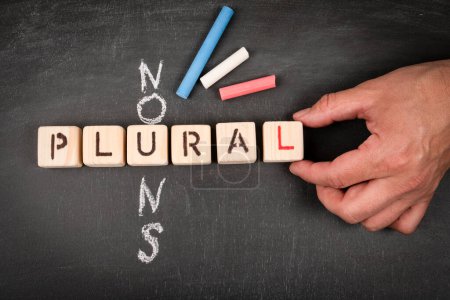 Plural nouns. Wooden block crossword puzzle and pieces of chalk on a chalkboard background.