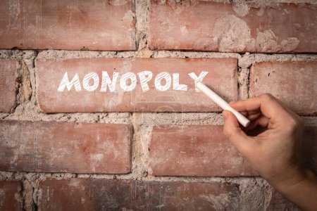 Monopoly. Text geschrieben mit weißer Kreide auf rotem Backsteinhintergrund.
