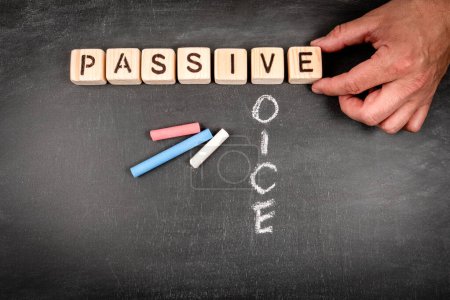 Passive voice. Wooden block crossword puzzle and pieces of chalk on a chalkboard background.