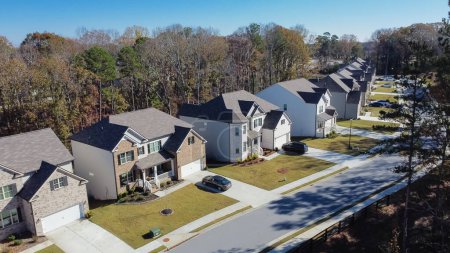 Close-up aerial view new development two story houses with two car garage drive way in Flowery Branch, Georgia, USA. Upscale residential neighborhood surrounded lush green tree fall foliage