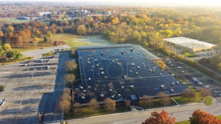 Foto de Large commercial building in woodland area with colorful fall foliage and rooftop units HVAC system provide heating, cooling, and ventilation in Pittsford, New York, USA. Aerial view industrial zone - Imagen libre de derechos
