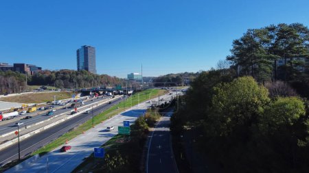 Téléchargez les photos : Arbre vert luxuriant le long de la route de service et circulation achalandée sur l'Interstate 285 (le Périmètre) avec des bâtiments du centre-ville d'Atlanta en arrière-plan, Géorgie, États-Unis. Vue aérienne autoroute moderne voies multiples - en image libre de droit
