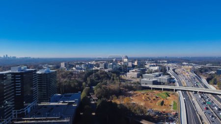 Téléchargez les photos : Autoroute périphérique occupée ou autoroute Interstate 285 avec immeubles de bureaux Périmètre Center et fond skylines du centre-ville d'Atlanta sous un ciel bleu clair. Tours de vue aérienne et chantier de construction - en image libre de droit