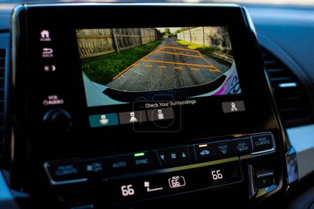 Großer Touchscreen mit Backup-Kamera und AC-Temperatur im Inneren moderner Minivans, digitale Anzeige zeigen Leitlinien und Holzzaun entlang der Hintergasse der Wohnstraße. Fahrassistenztechnik