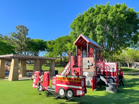 Photo for Themed firetruck playground with pergola picnic table, green artificial grass turf carpet, tall trees under clear blue sky in Carrollton, suburbs Dallas, Texas, USA. Large recreational place for kids - Royalty Free Image