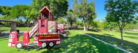 Photo for Panorama view firetruck themed playground with green artificial grass turf carpet by tall mature trees clear blue sky in Carrollton, suburbs Dallas, Texas, USA. Large recreational place for kids - Royalty Free Image