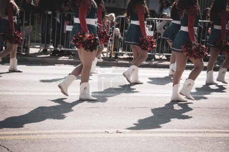 Foto de Foto de tono diverso grupo de jóvenes animadoras en faldas azules de vacaciones, botas blancas, pompones de aluminio bailando en la calle con multitud detrás de barricadas de acero del centro de Dallas, desfiles de Texas. Concepto Rally - Imagen libre de derechos