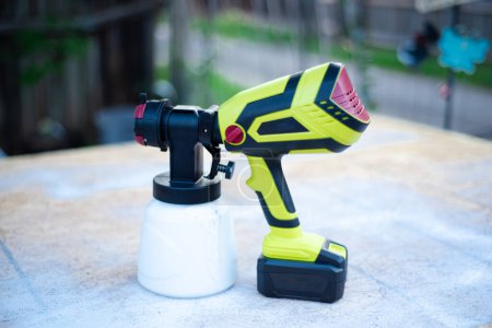 Photo for Outdoor painting with battery powered cordless paint sprayer gun on wooden oriented strand board OSB board, concrete back alley wooden fence background. Handy power tool for painting job - Royalty Free Image