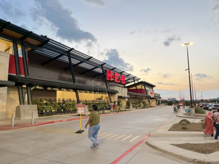 Photo for PLANO, TX, USA-JULY 8, 2023: Customer entering the facade entrance of recently opened H-E-B Grocery Company franchise supermarket chain with busy traffic at sunset. DFW Metroplex shopping location - Royalty Free Image