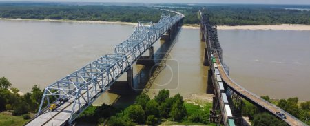 Téléchargez les photos : Panorama Pont de Vicksburg et Vieux Pont de Vicksburg avec train de marchandises traversant la rivière ferme ferroviaire entièrement en acier transportant l'Interstate 20, U.S. Route 80 à travers le ciel ensoleillé du fleuve Mississippi. Vue aérienne - en image libre de droit