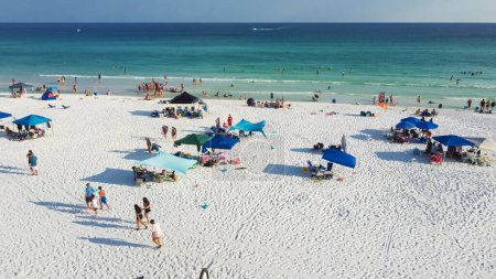 Téléchargez les photos : Groupe de personnes marchant le long des plages de sable blanc sucré à côté du parapluie coloré couronné le long de l'eau turquoise, de magnifiques vagues bleues ombragées à la plage de Miramar, South Walton, Floride, États-Unis. Vue aérienne - en image libre de droit