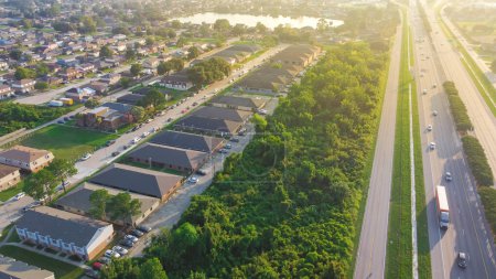 Photo for Busy traffic on Interstate 10 highway near Lake Barrington early morning along row of townhouses, condos, lush green trees and residential units in Little Woods, Eastern New Orleans. Aerial Louisiana - Royalty Free Image