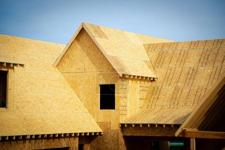 Téléchargez les photos : Maison en bois en forme de L avec toit lucarne à pignon en construction, enveloppe en contreplaqué de panneaux orientés (OSB) dans les banlieues Atlanta, Géorgie, États-Unis. Charpente poutre nouvelle maison de développement - en image libre de droit