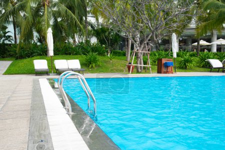 Foto de Barandilla de la piscina en el complejo de lujo con fila de sillas tumbonas cojín blanco, sombrilla de playa colapsada, mesa de taburete redonda, rodeada de palmeras de coco, jardín tropical en Nha Trang, Vietnam. Viajes - Imagen libre de derechos