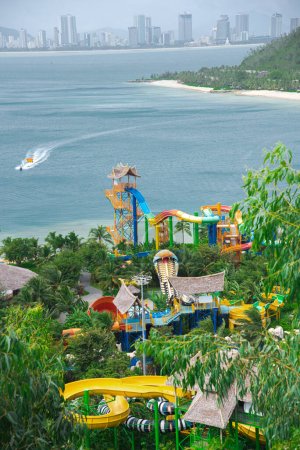 Téléchargez les photos : Parc aquatique à thème tropical avec le centre-ville de Nha Trang skylines fond de chaîne de montagnes, vue aérienne aquapark familial coloré, longues promenades toboggans arbre vert luxuriant, rivage sablonneux, sports de plage. Viêt Nam - en image libre de droit