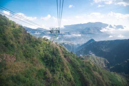 Vista panorámica brumosa y soleada Cordillera Hoang Lien Son, Valle Muong Hoa, estructura de acero pilar de cable de pilar de pilar de teleférico de elevación aérea acarreado teleférico sobre el suelo, cielo azul nube, Sapa. Vietnam
